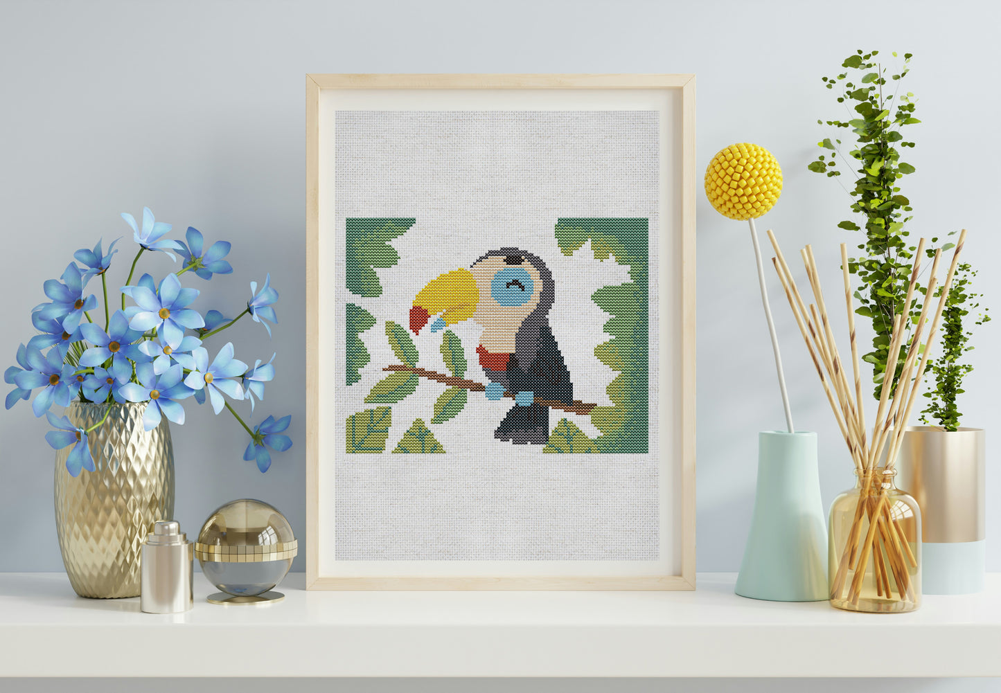 Framed cross-stitch art of a toucan on a shelf with decorative items.