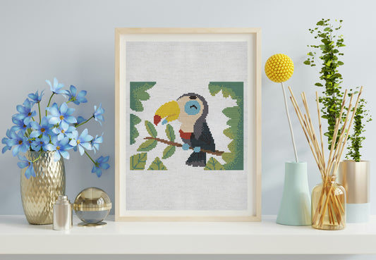 Framed cross-stitch art of a toucan on a shelf with decorative items.
