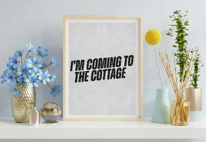 Framed print with 'I'm Coming to the Cottage' text on a shelf with decorative items.