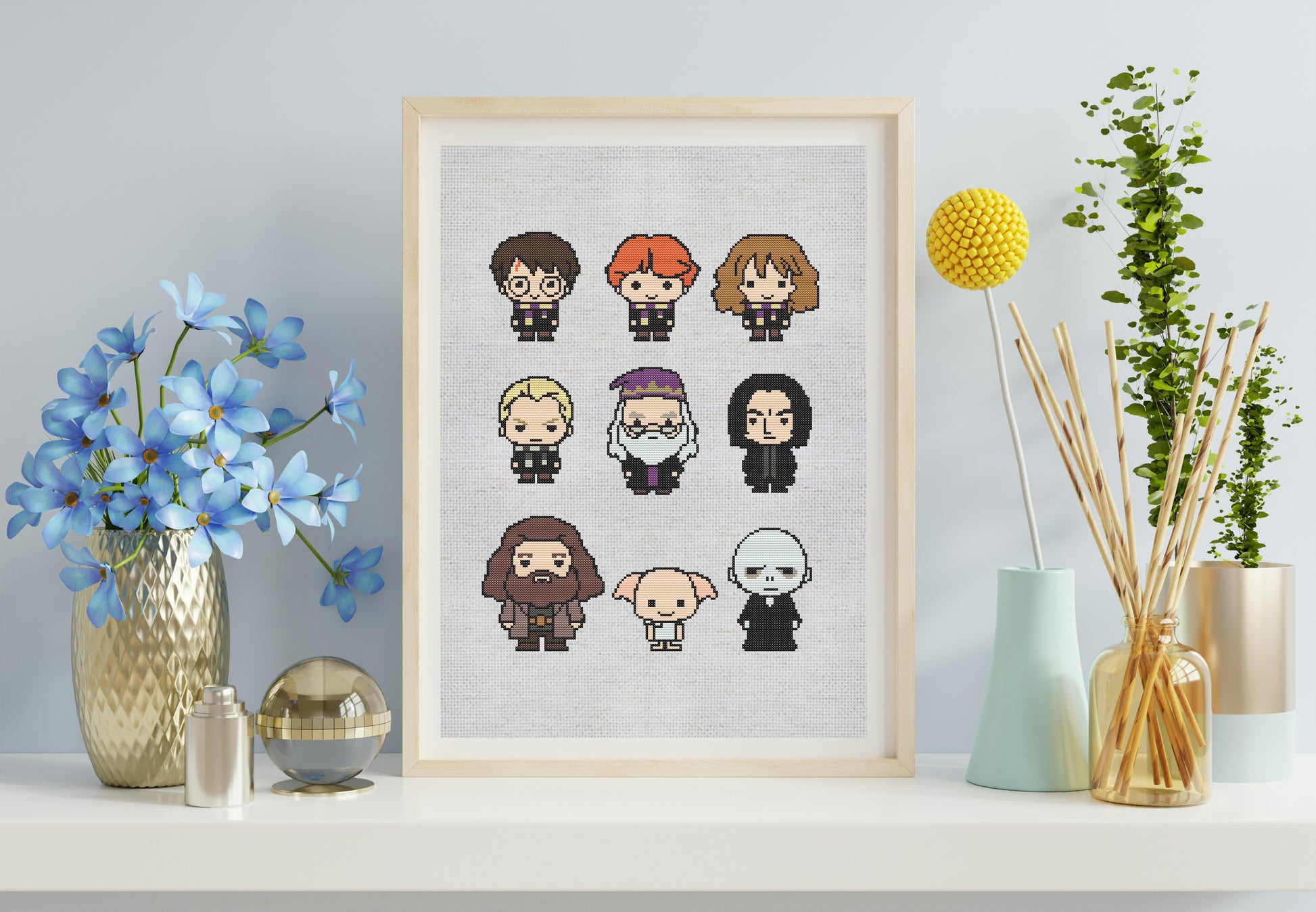 Framed cross-stitch art of cartoon characters on a shelf with decorative items.