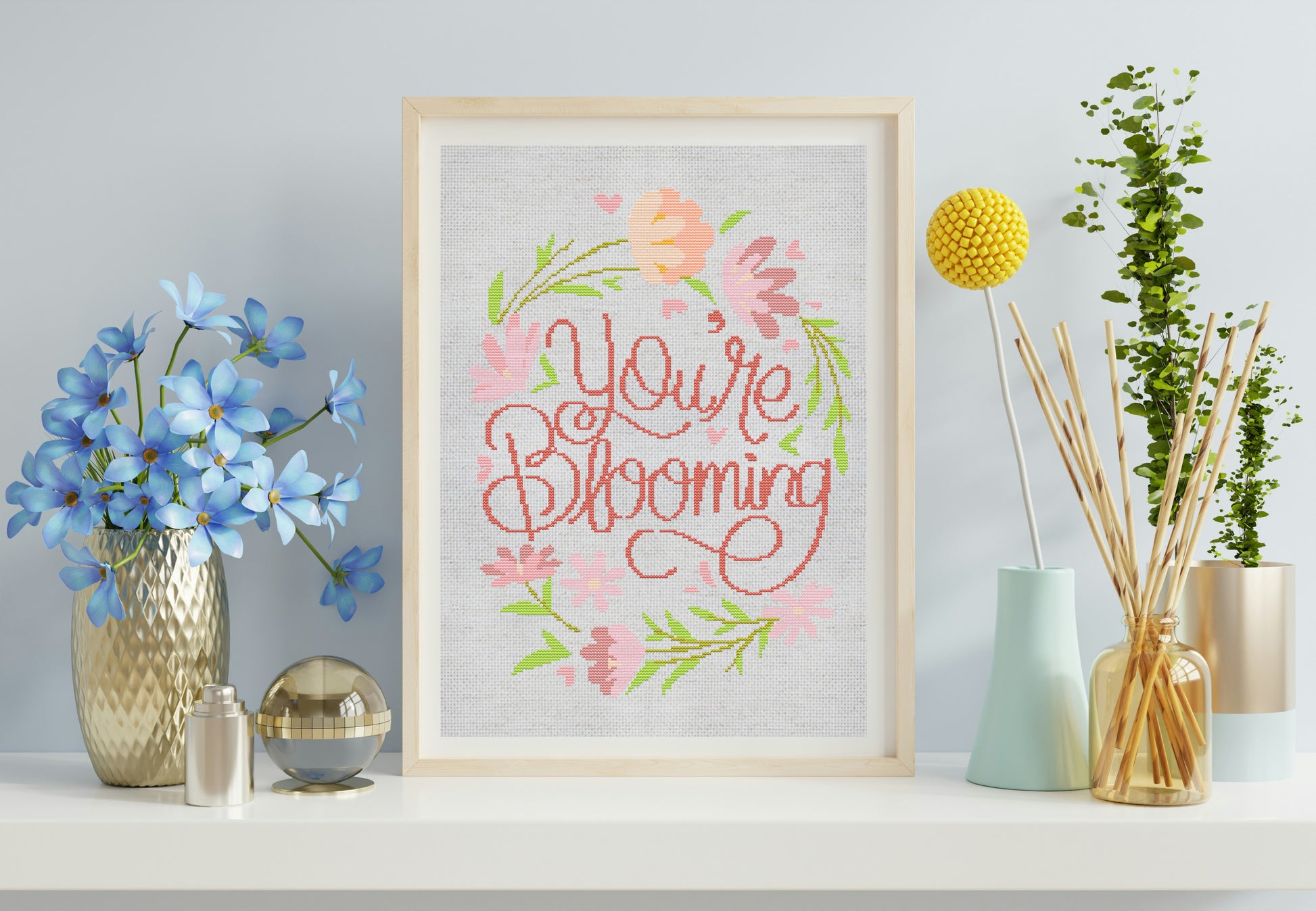 Framed artwork with 'You're Blooming' text and floral design on a shelf with decorative items.