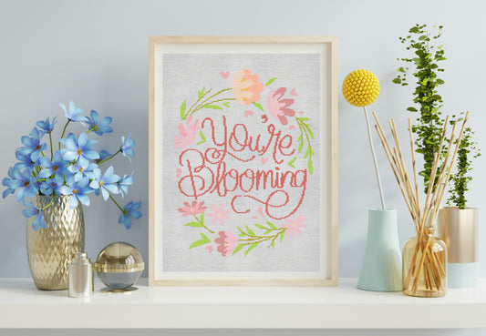 Framed artwork with 'You're Blooming' text and floral design on a shelf with decorative items.