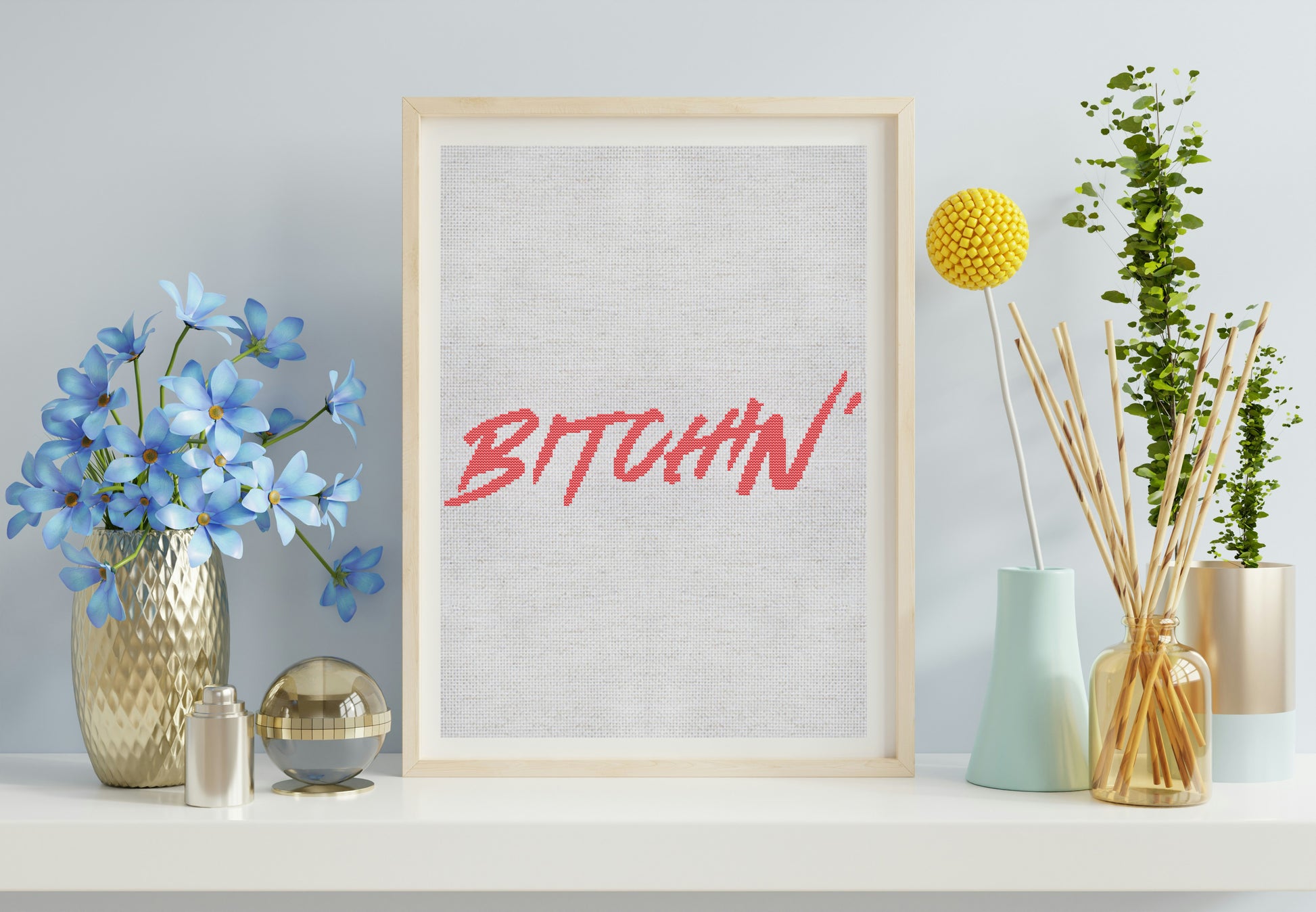 Framed artwork with the word 'BITCHIN'' on a shelf with decorative items.