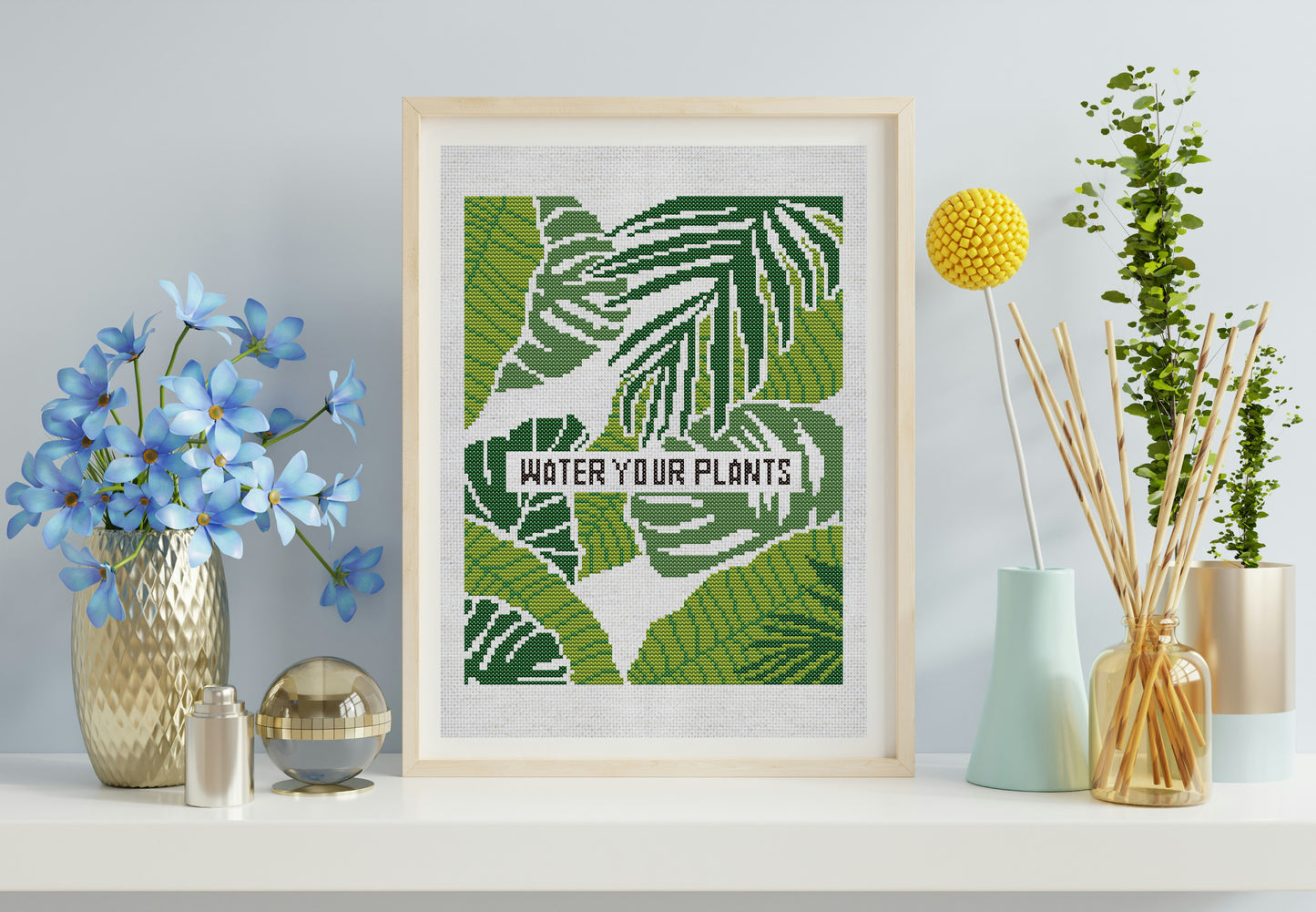 Framed artwork with leaf design and 'Water Your Plants' text, placed on a surface with decorative items.