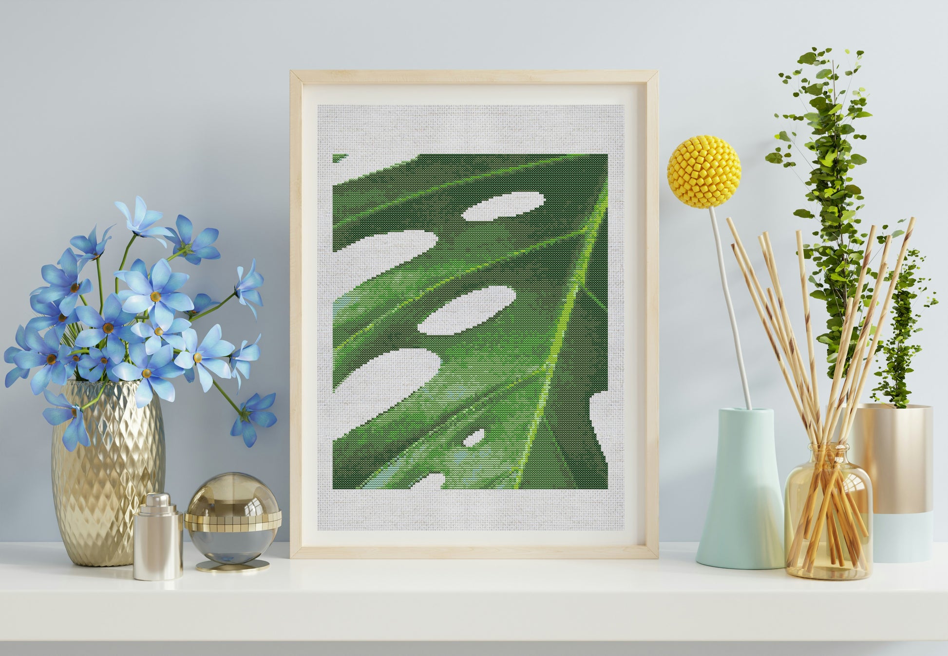 Framed artwork of a green leaf with white spots on a shelf with decorative items.
