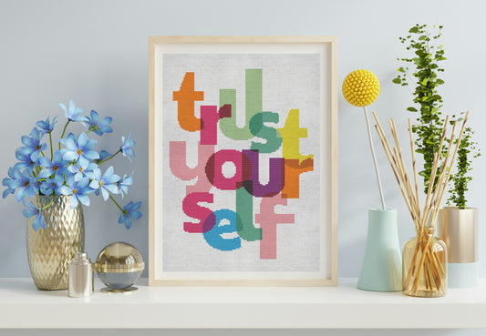 Framed artwork with colorful letters spelling 'Trust Yourself' on a shelf with decorative items.