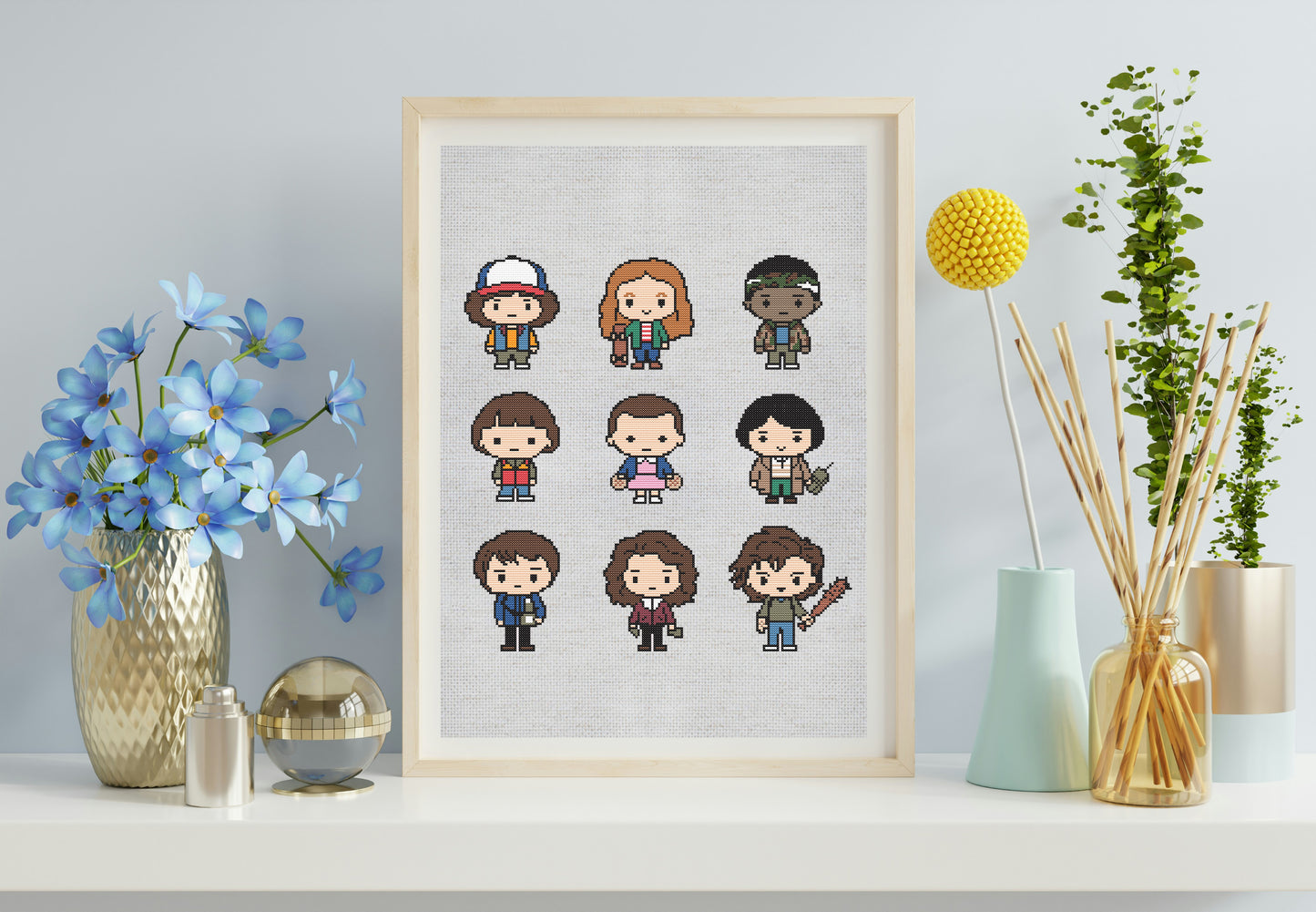 Framed cross-stitch art of cartoon characters on a wall with decorative items.