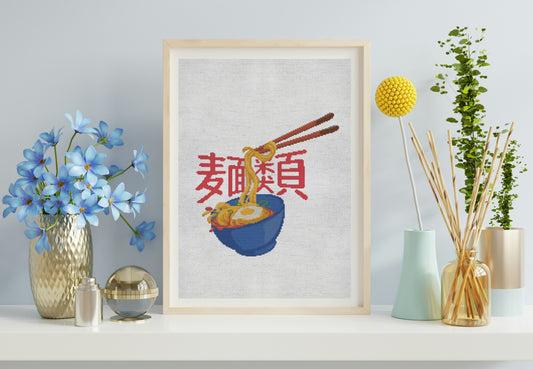Framed cross-stitch art of a bowl of noodles with chopsticks on a shelf with decorative items.