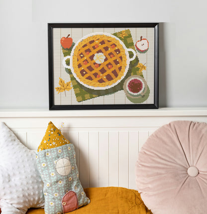 Framed cross-stitch art of a waffle with fruit on a wall above a sofa with decorative pillows.