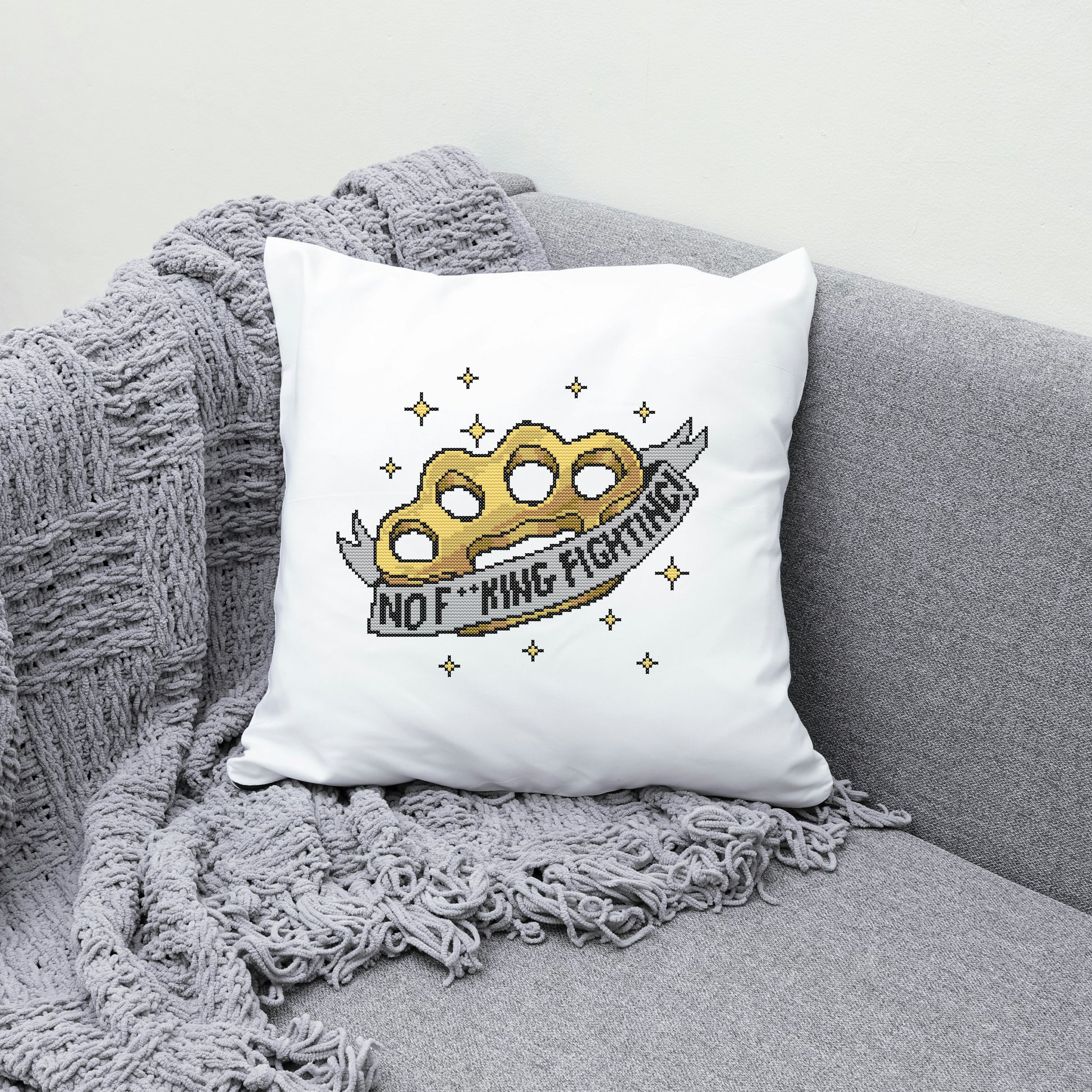 White pillow with a gold knuckle duster design and text on a gray couch.