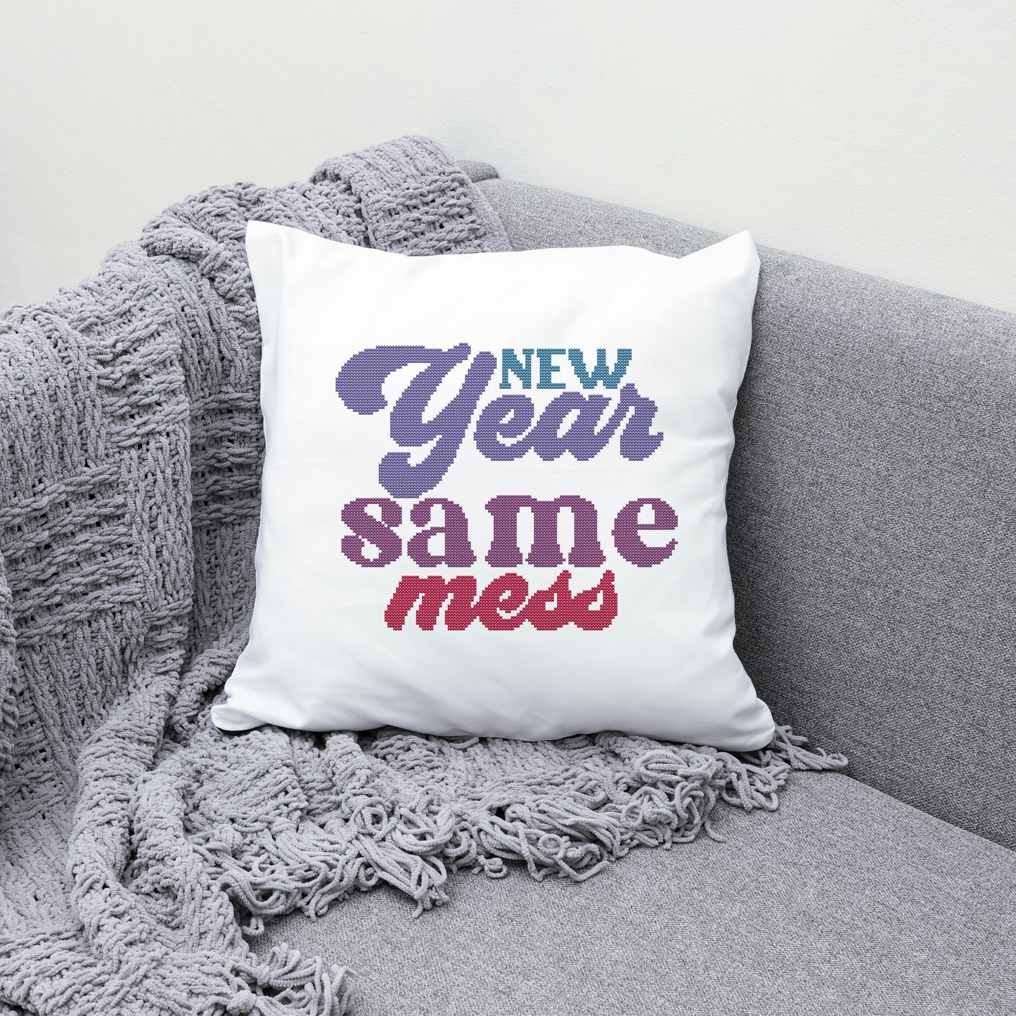 White pillow with 'New Year same mess' text on a gray couch with a textured blanket.