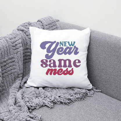 White pillow with 'New Year same mess' text on a gray couch with a textured blanket.