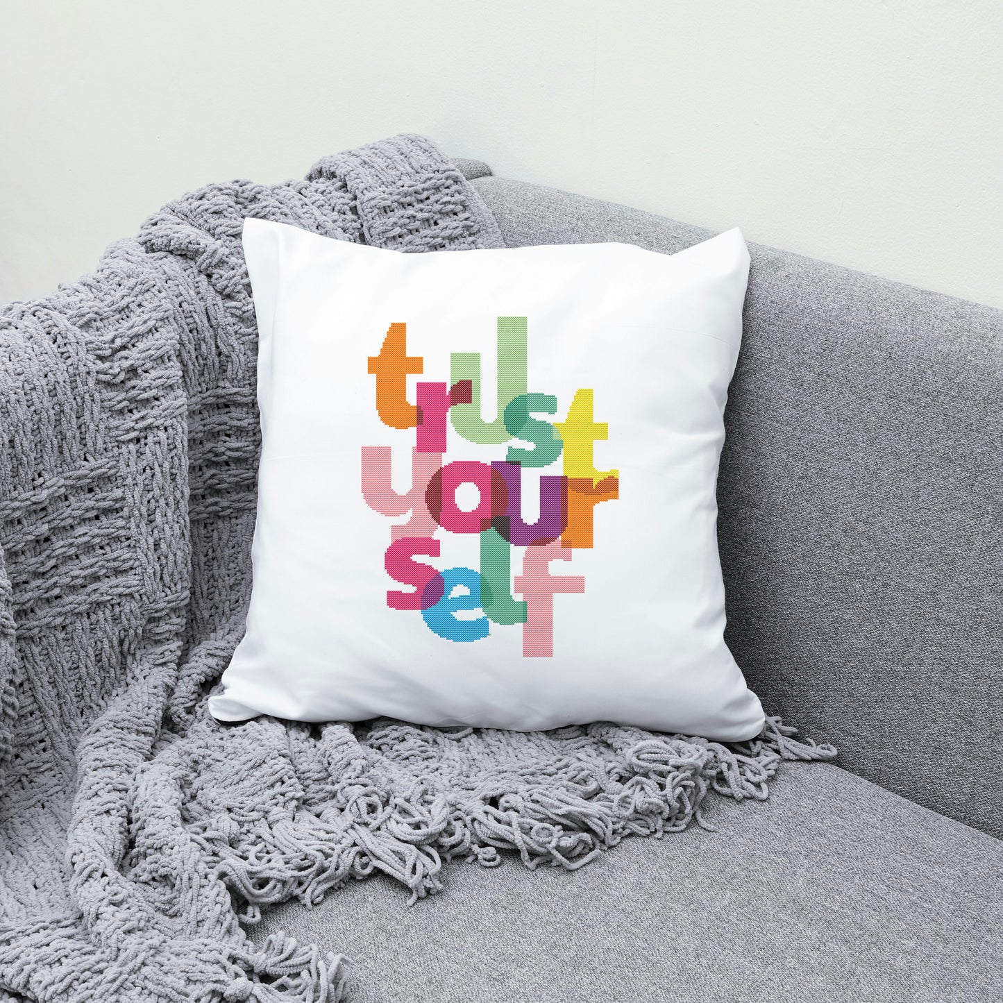 White pillow with colorful text 'Trust Yourself' on a gray couch with a gray blanket.