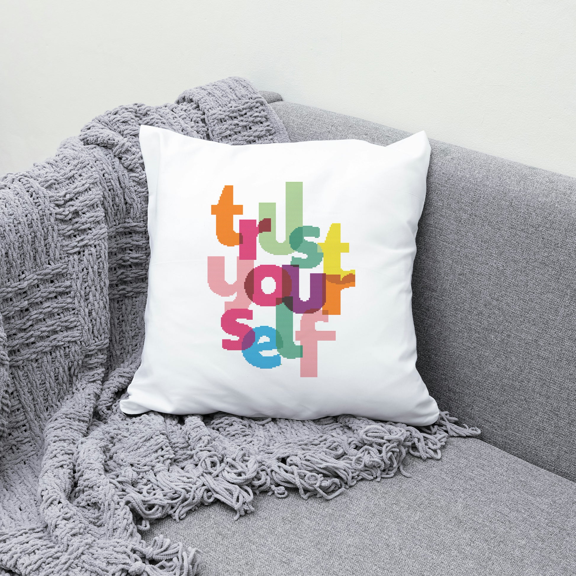 White pillow with colorful text 'Trust Yourself' on a gray couch with a gray blanket.