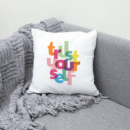 White pillow with colorful text 'Trust Yourself' on a gray couch with a gray blanket.