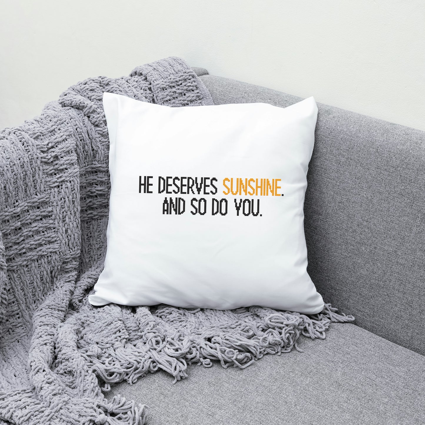 White pillow with text on a gray couch with a blanket