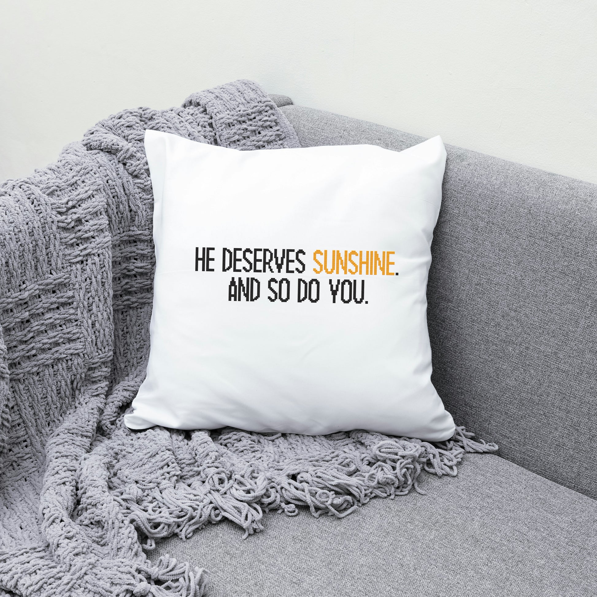 White pillow with text on a gray couch with a blanket