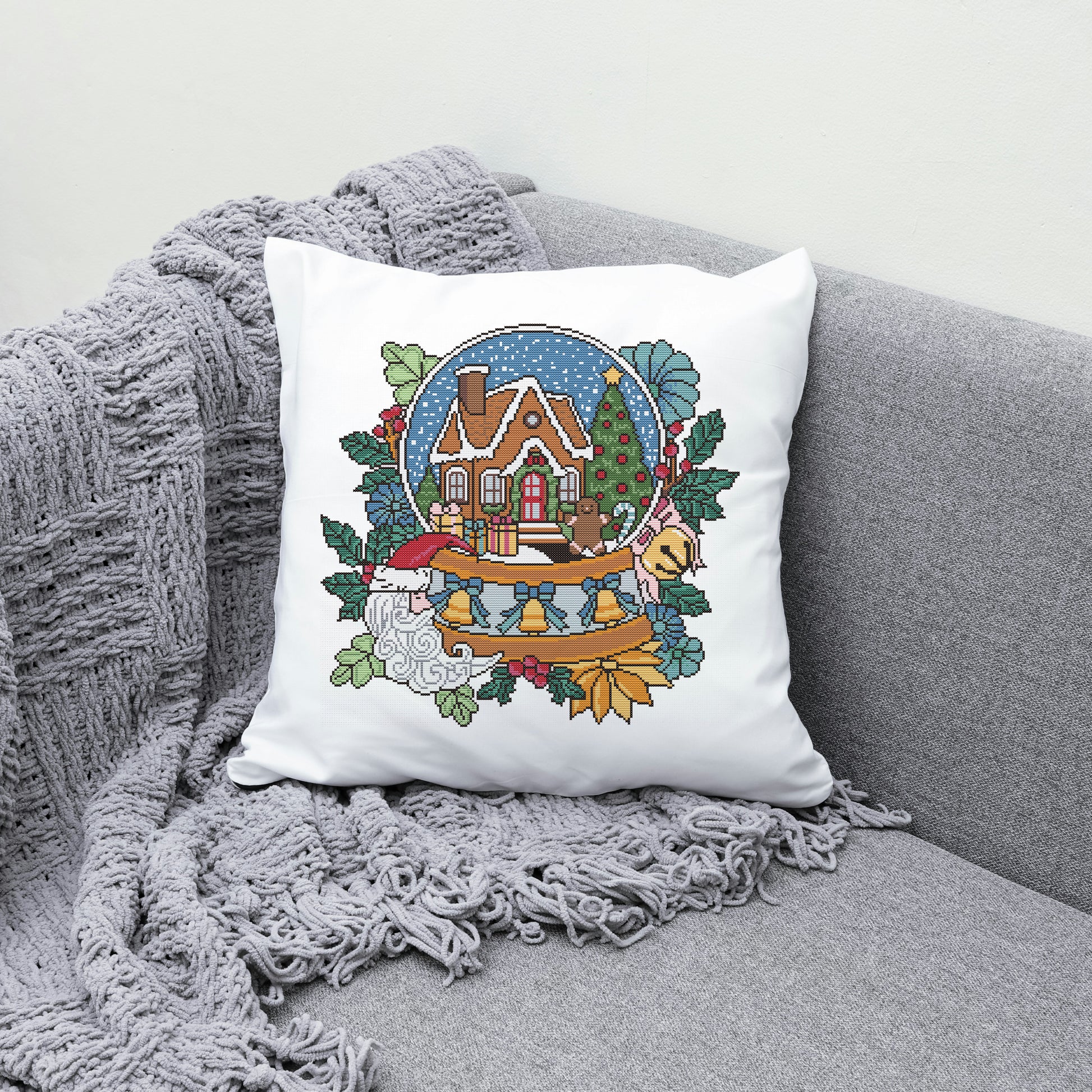 Decorative pillow with a Christmas design featuring a house, trees, and a gnome on a gray couch.