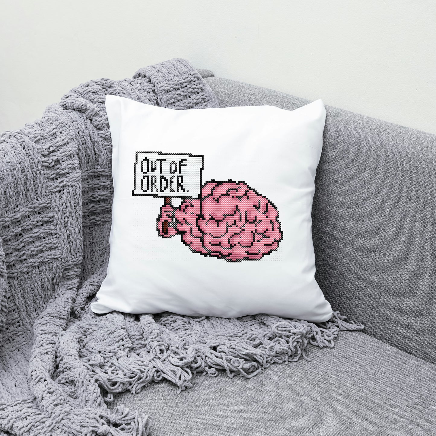 White pillow with pink brain design and 'Out of Order' text on a gray couch.