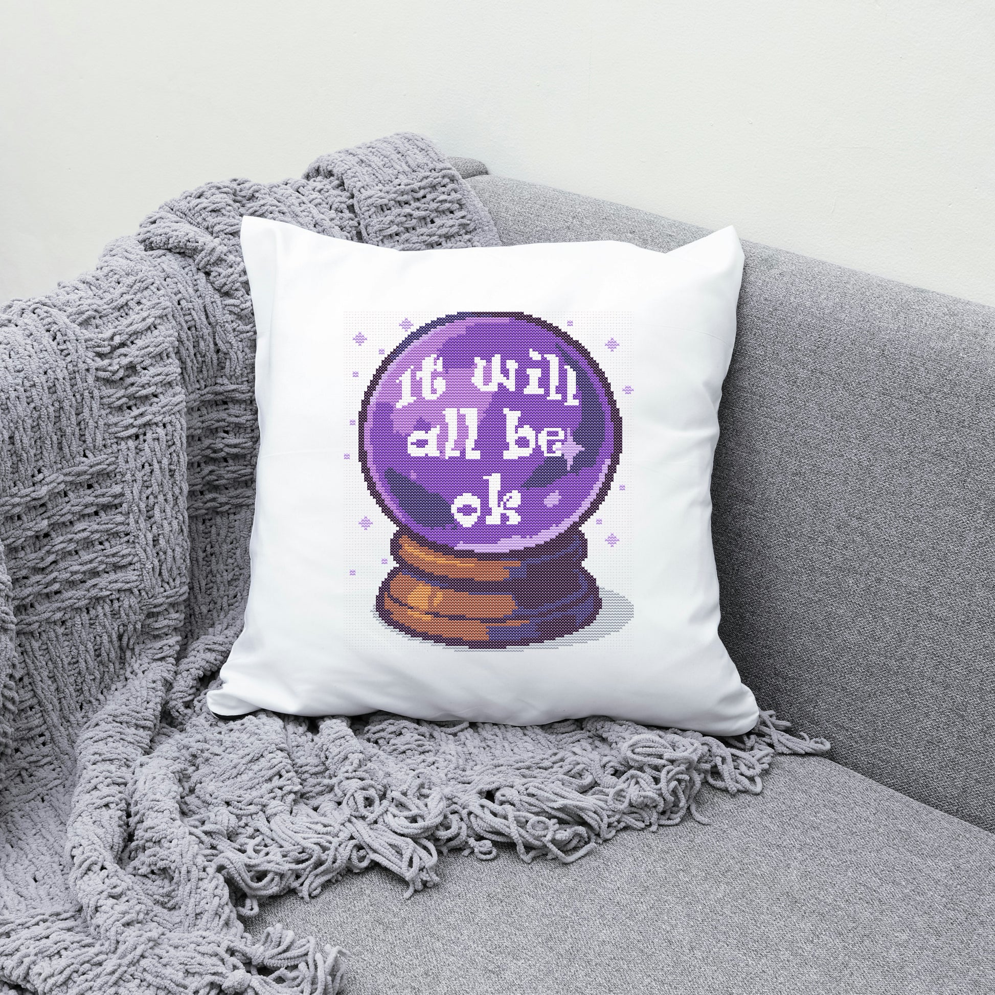Decorative pillow with a crystal ball design and 'It will all be ok' text on a gray couch.