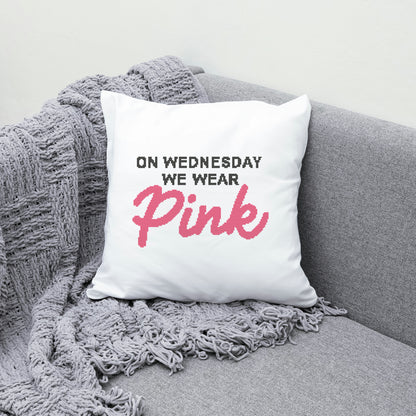 White pillow with text 'On Wednesday We Wear Pink' on a gray couch with a gray blanket.