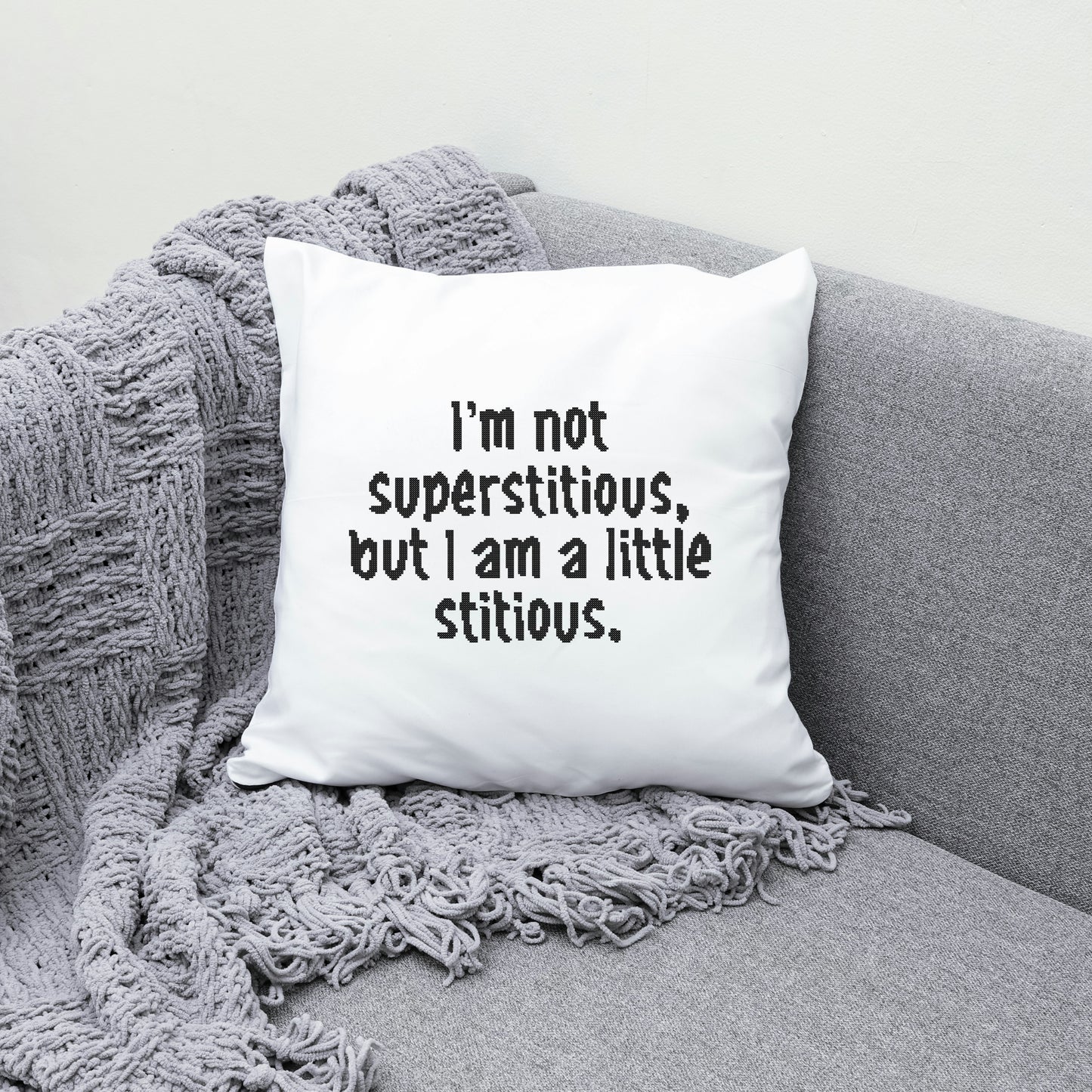 White pillow with humorous text on a gray couch with a textured blanket.