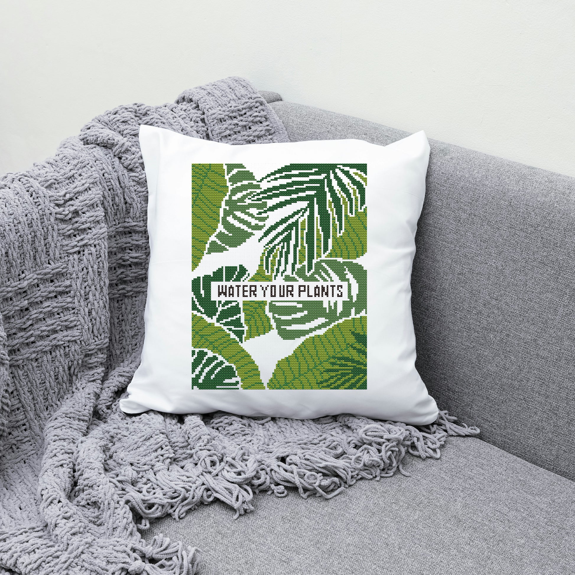 Decorative pillow with leaf pattern and text 'Water Your Plants' on a gray couch.