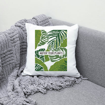 Decorative pillow with leaf pattern and text 'Water Your Plants' on a gray couch.