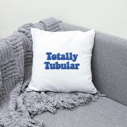 White pillow with 'Totally Tubular' text on a gray couch with a textured blanket.