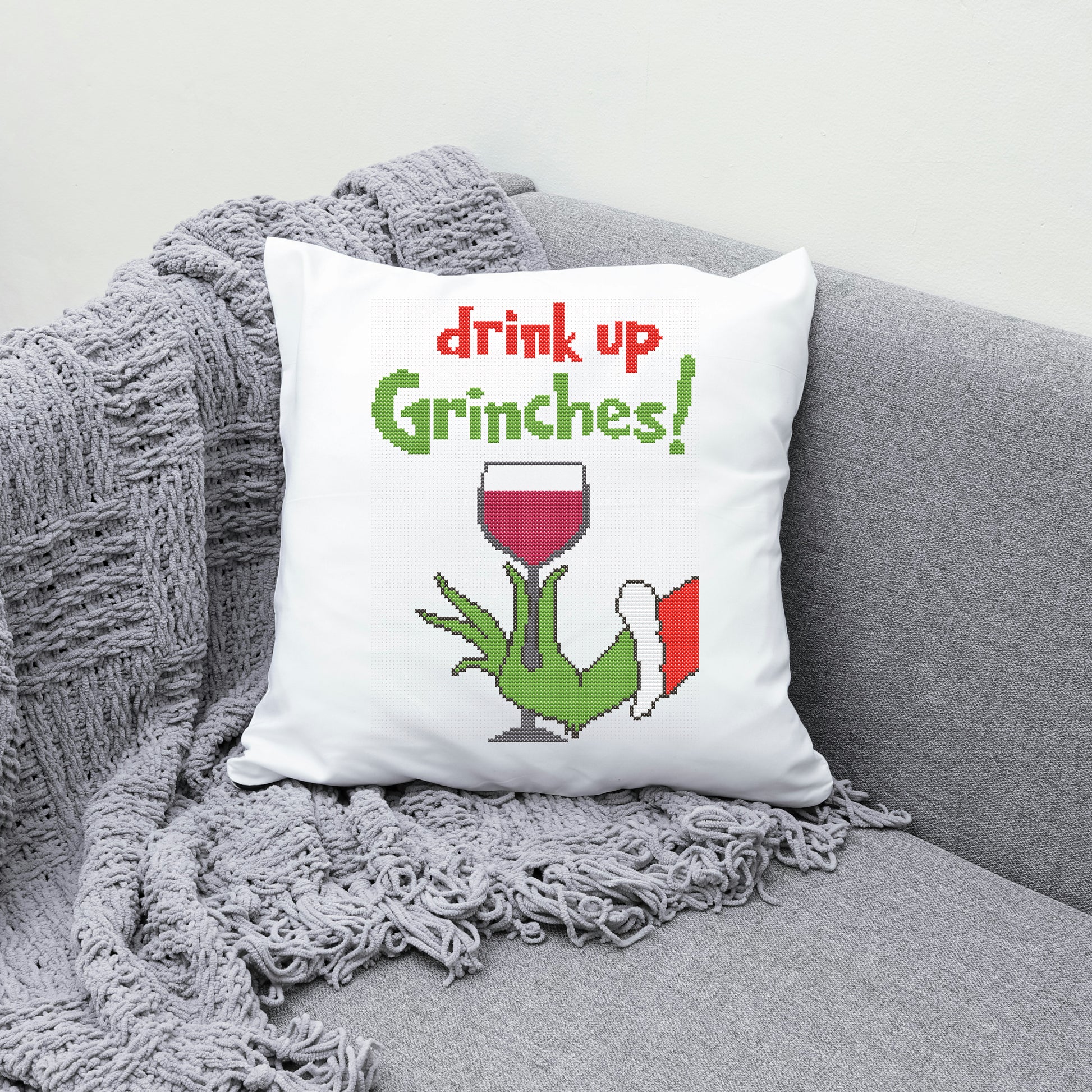 Decorative pillow with 'drink up Grinches!' text and a Grinch holding a wine glass on a gray couch.