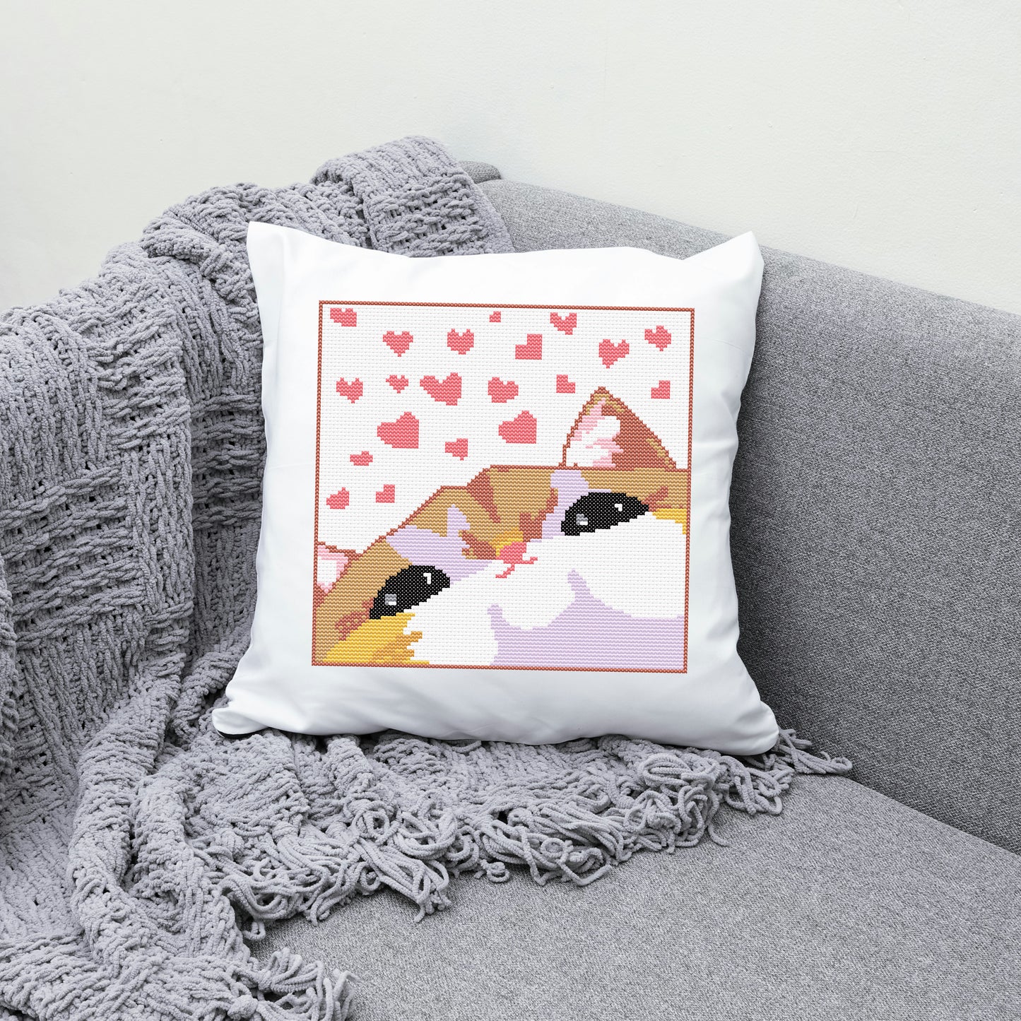 Pillow with a cat design and heart pattern on a gray couch.