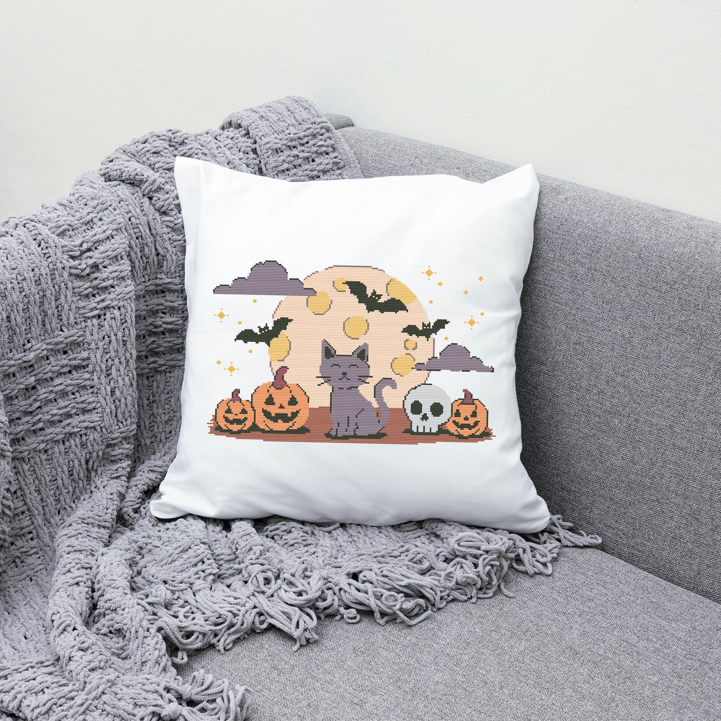 Halloween-themed pillow with a cat, pumpkins, and skull design on a gray couch.