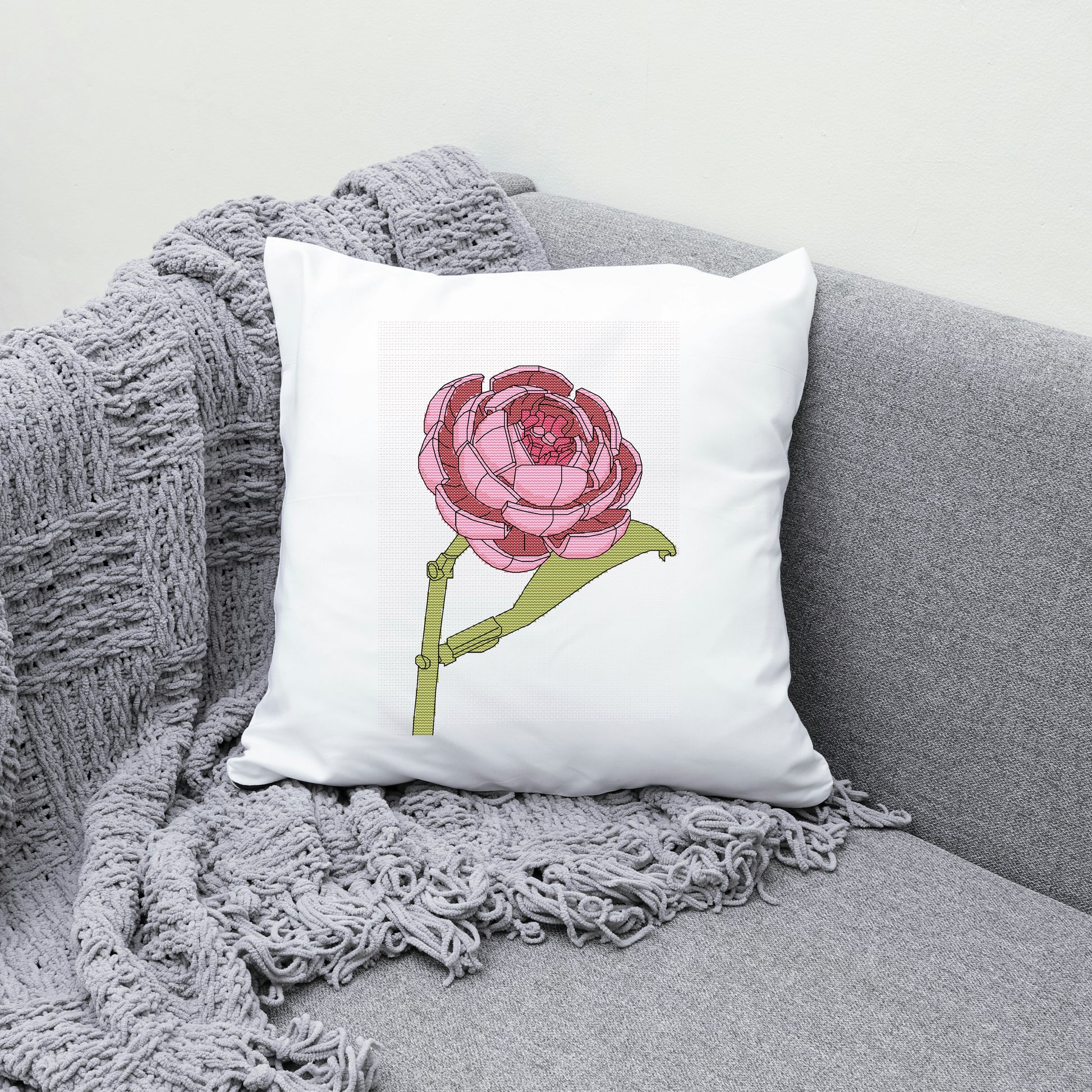 White pillow with a pink flower design on a gray couch with a gray blanket.