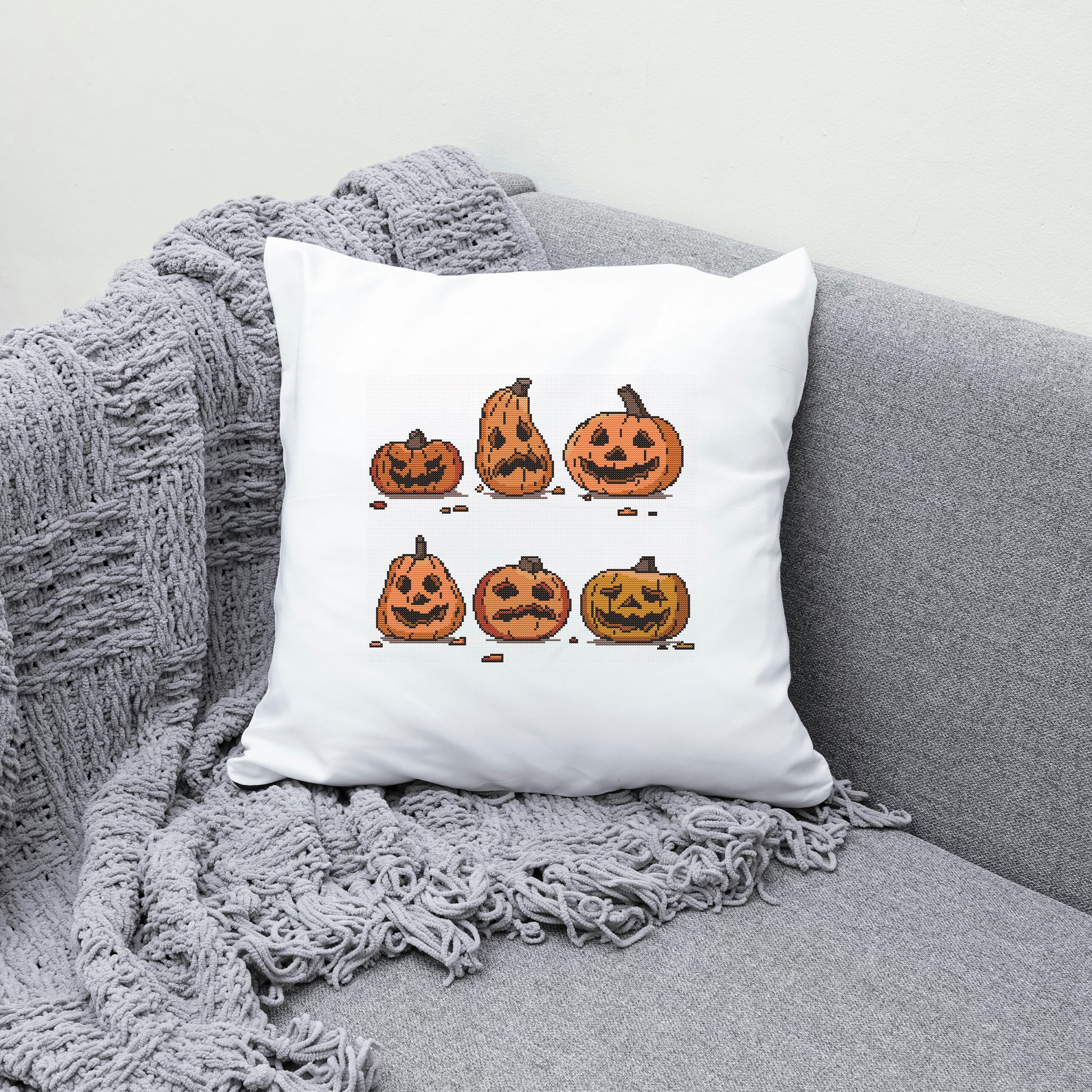 White pillow with Halloween-themed pumpkins design on a gray couch.