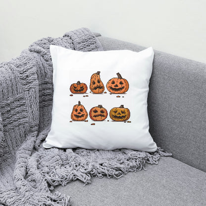 White pillow with Halloween-themed pumpkins design on a gray couch.