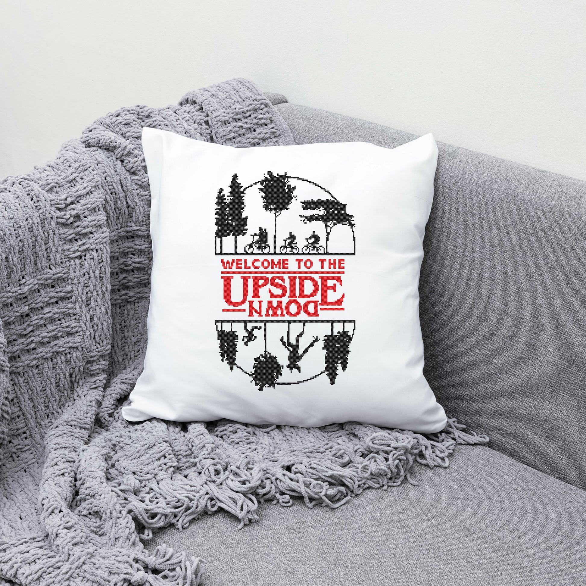 White pillow with 'Welcome to the Upside Down' design on a gray couch.