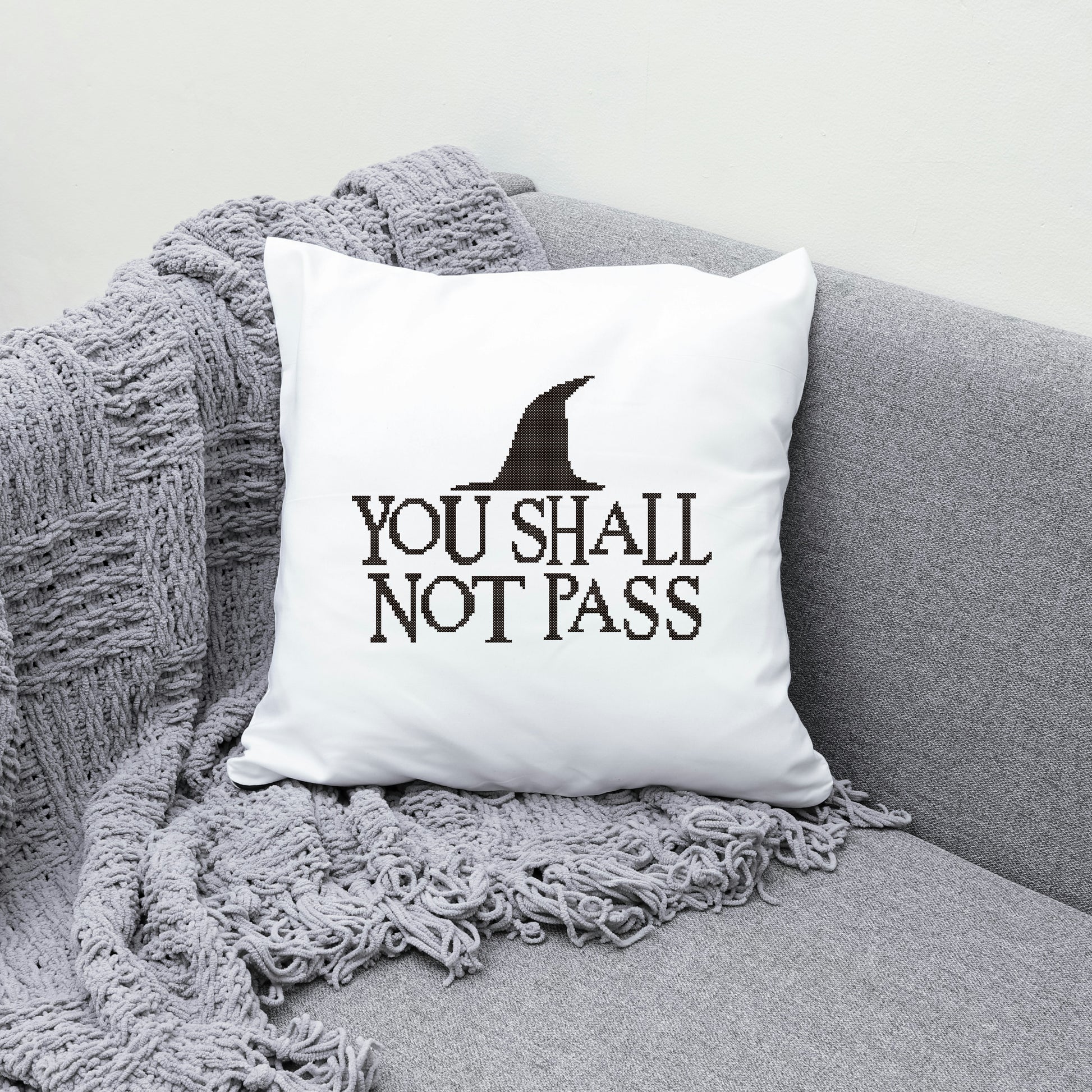 White pillow with 'You Shall Not Pass' text on a gray couch with a textured blanket.