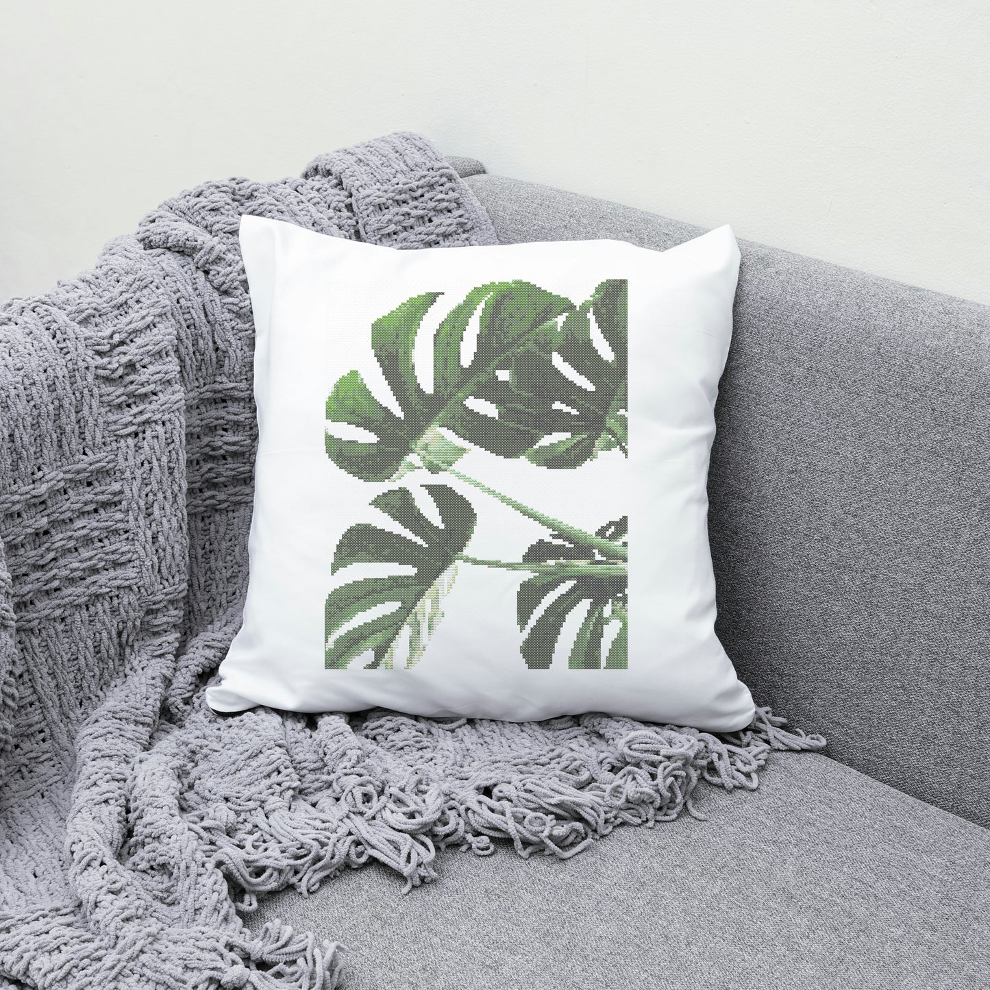 White pillow with green leaf design on a gray couch with a gray blanket.