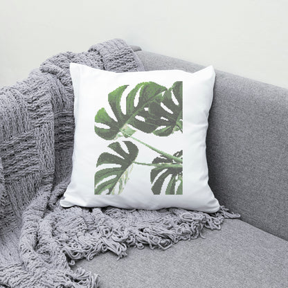 White pillow with green leaf design on a gray couch with a gray blanket.