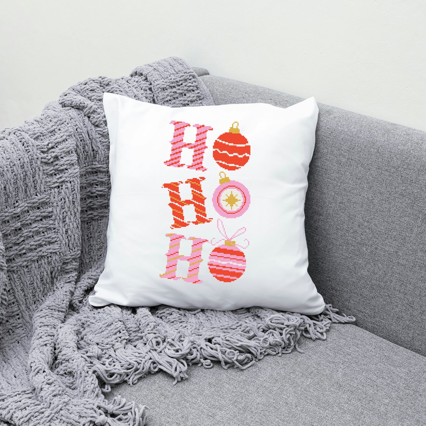 Decorative pillow with 'HO HO HO' and Christmas ornaments on a gray couch.