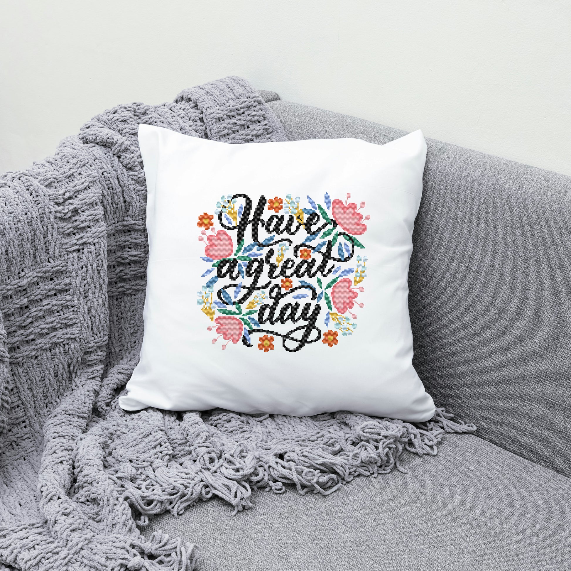 White pillow with 'Have a great day' text and floral design on a gray couch.