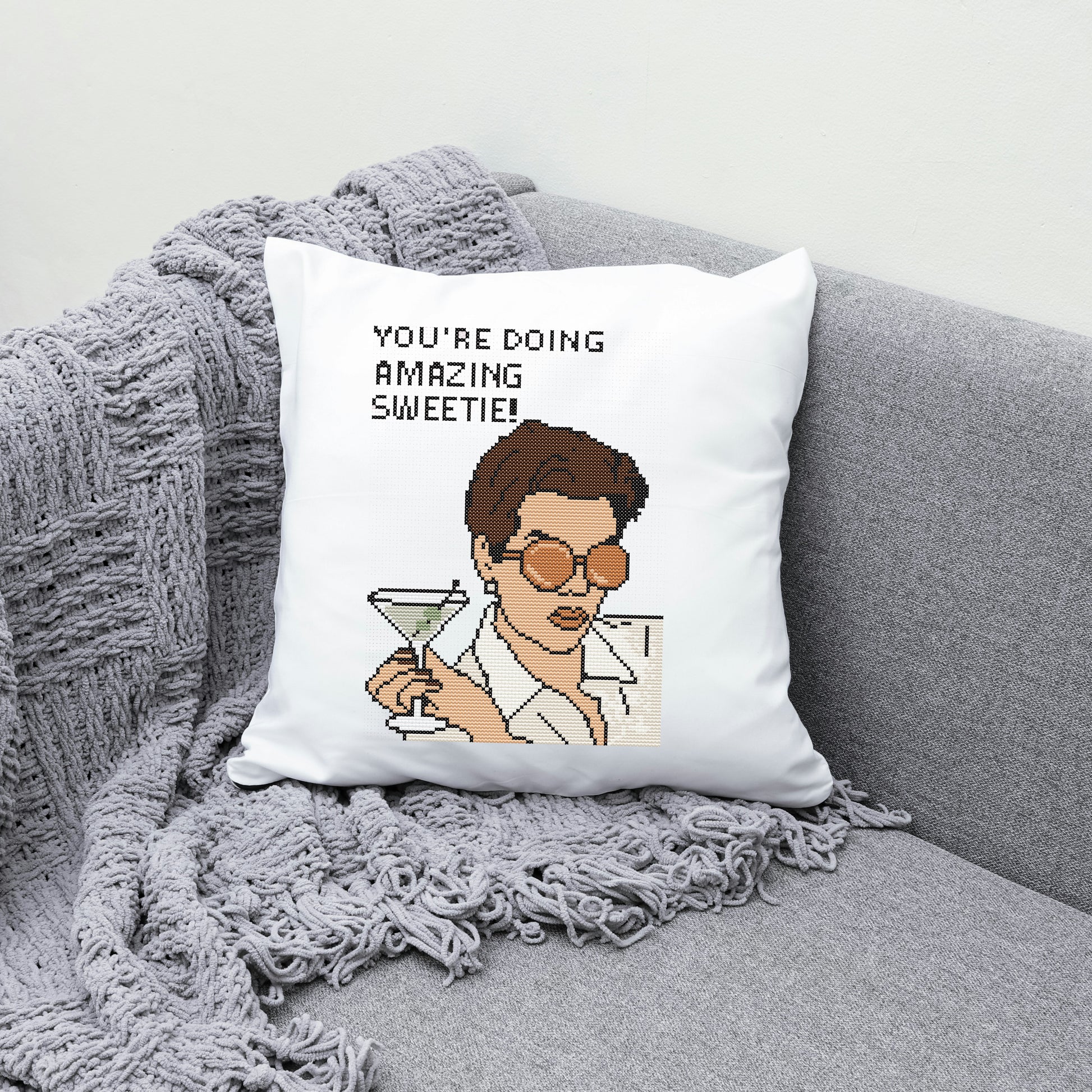 Pillow with a character holding a martini and text 'You're doing amazing, sweetie!' on a gray couch.