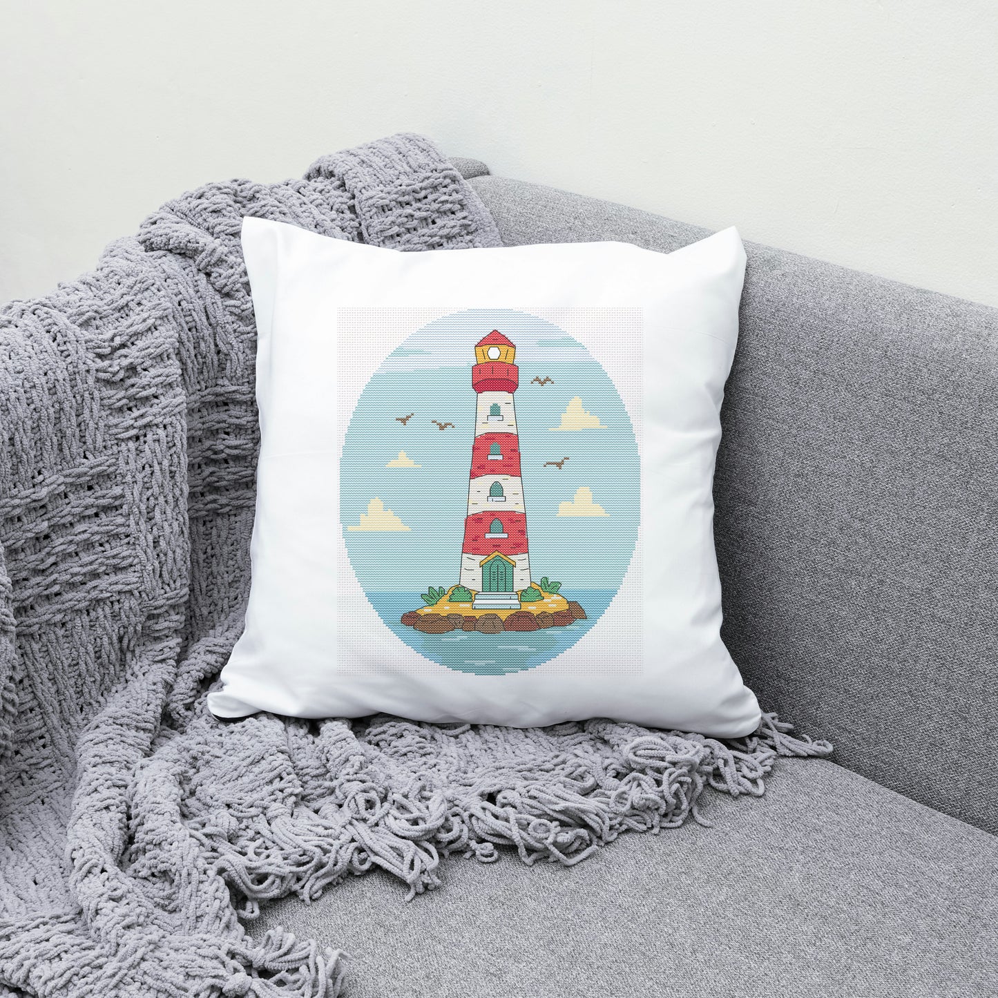 Decorative pillow with a lighthouse design on a gray couch with a blanket.