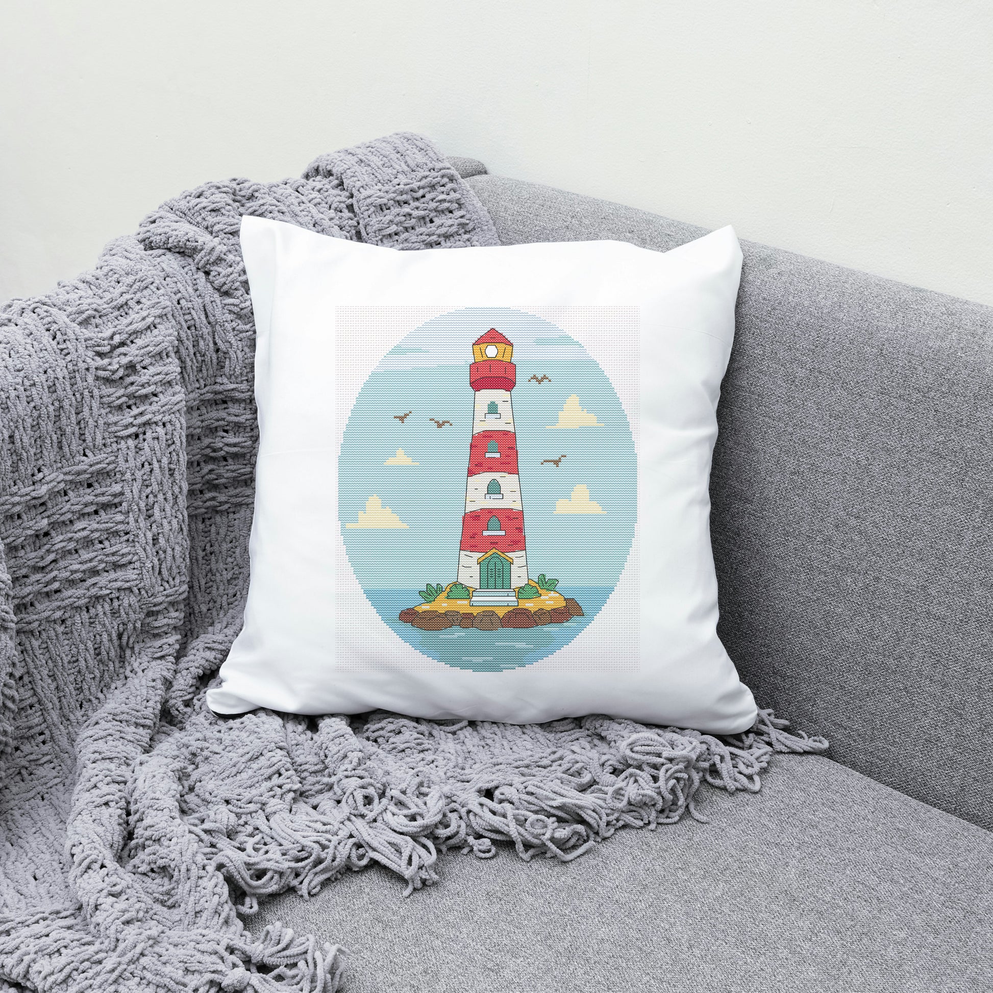Decorative pillow with a lighthouse design on a gray couch with a blanket.