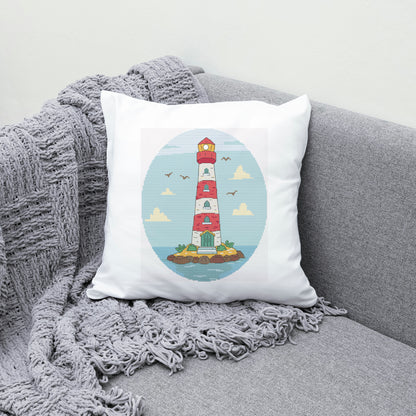 Decorative pillow with a lighthouse design on a gray couch with a blanket.
