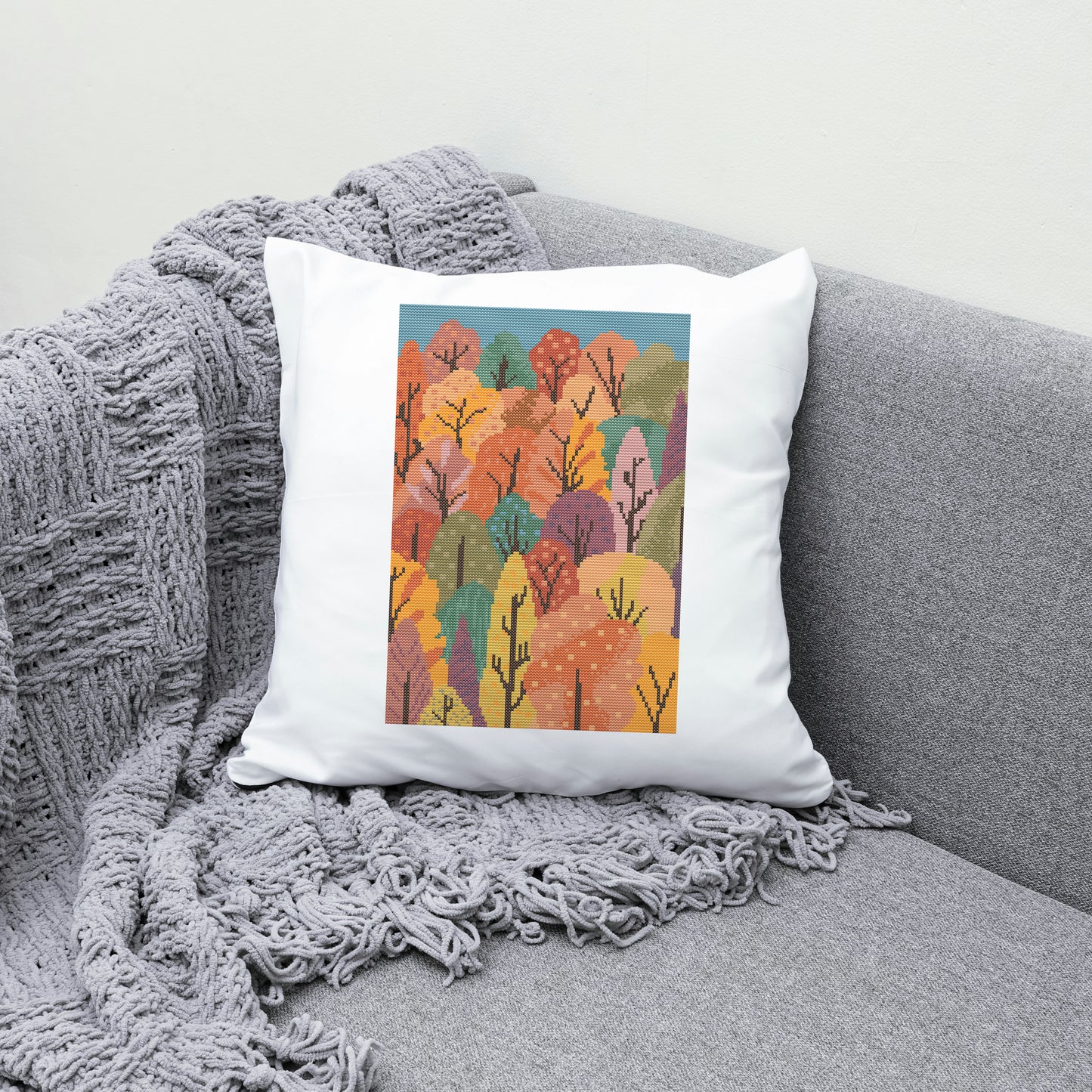 Decorative pillow with autumn tree design on a gray couch with a blanket.