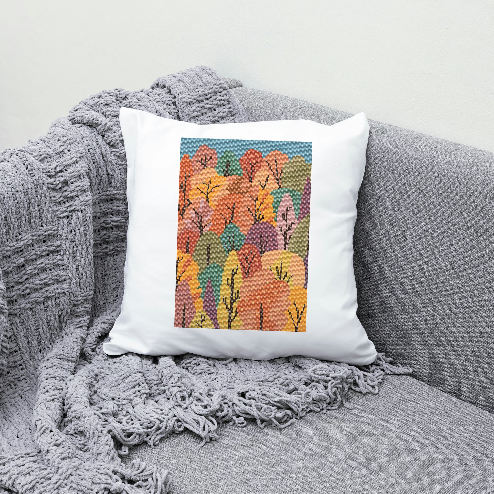 Decorative pillow with autumn tree design on a gray couch with a blanket.