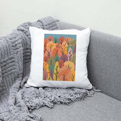 Decorative pillow with autumn tree design on a gray couch with a blanket.