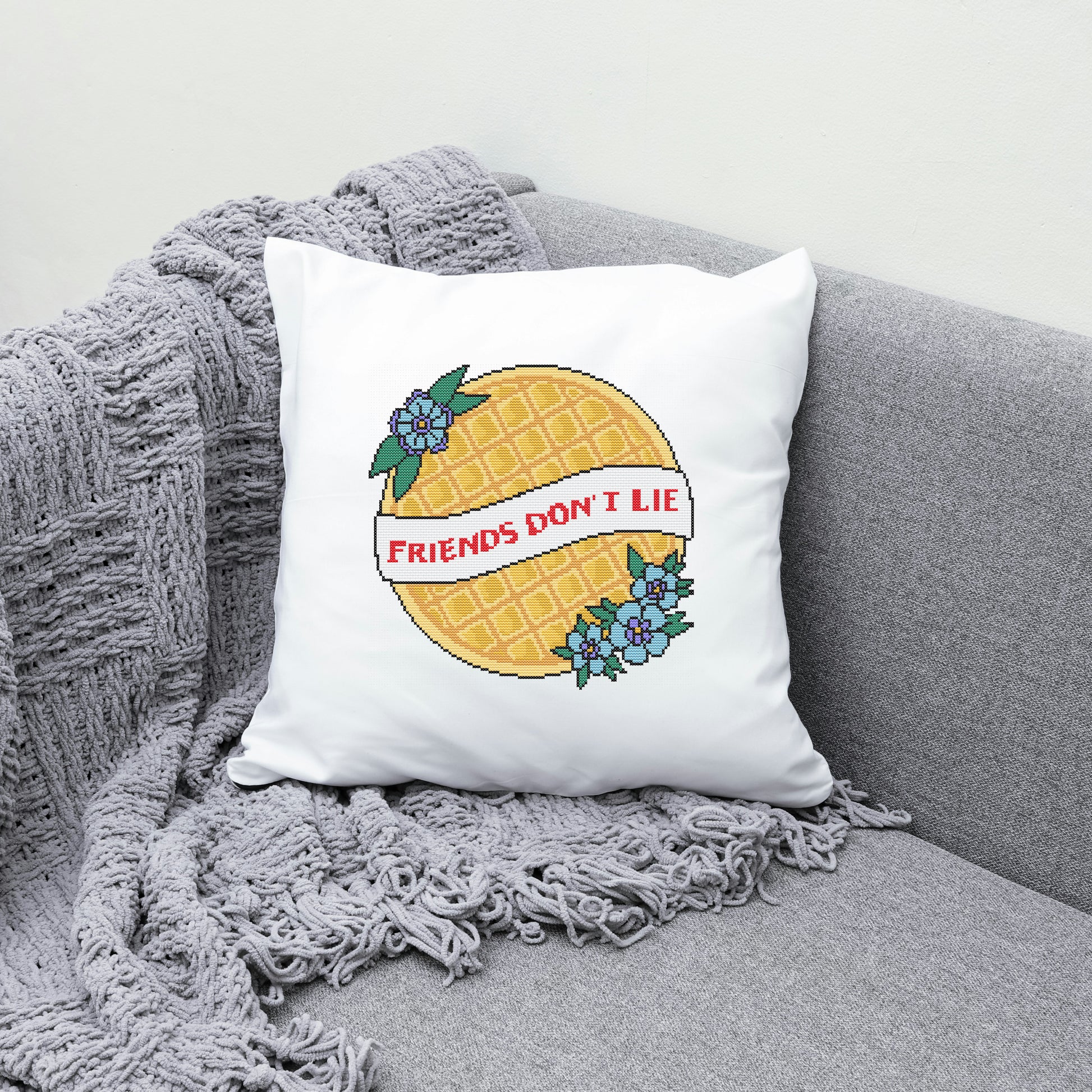 Pillow with pineapple design and 'Friends Don't Lie' text on a gray couch.