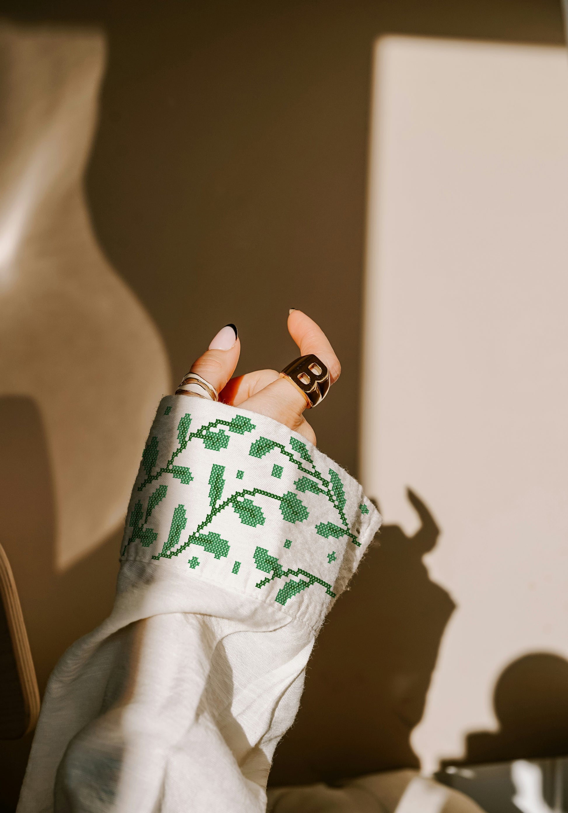 Hand wearing a white sleeve with green cross-stitch pattern, holding a phone.